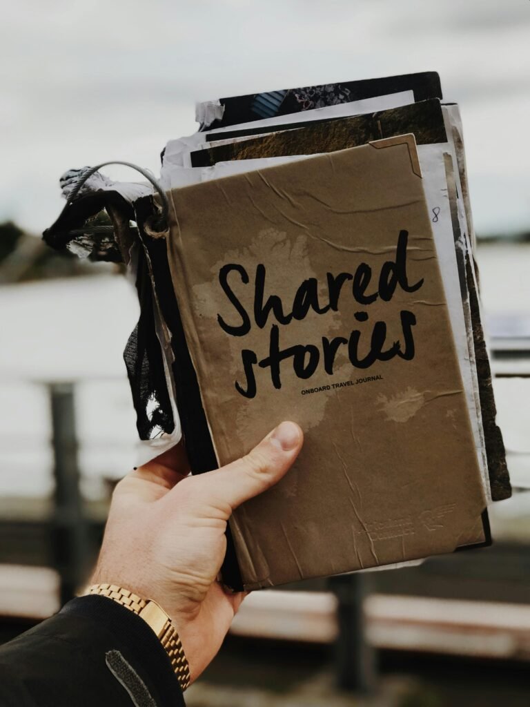 pexels-photo-2954199-2954199 Hand holds a "Shared Stories" journal against a blurred outdoor backdrop, emphasizing creativity and personal storytelling.